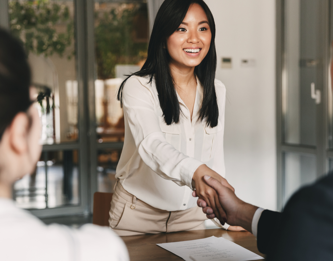 A smiling woman extending a handshake at a job interview