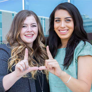 Two smiling women making a U shape with their hands